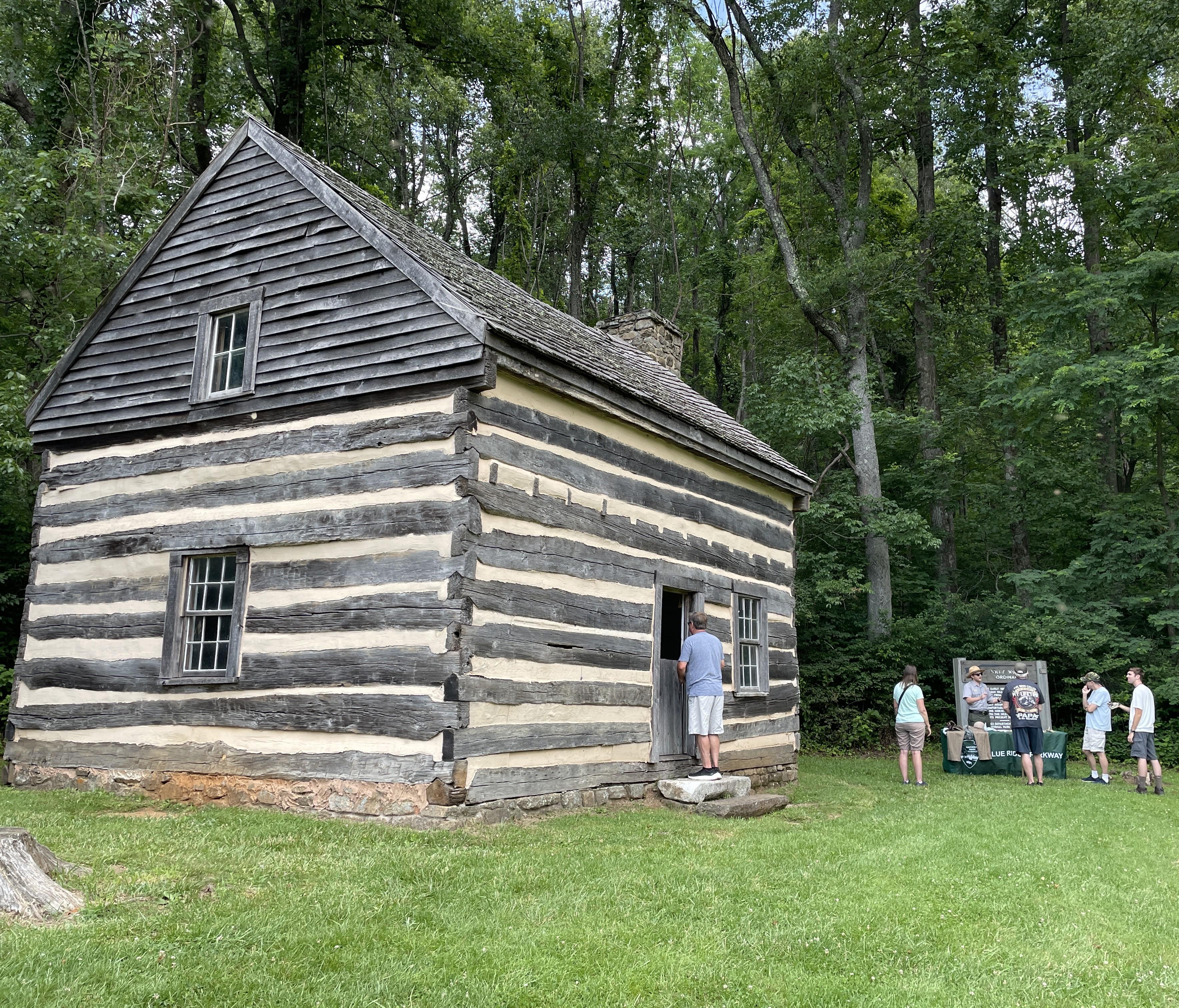 2-story cabin with a man looking in the doorway and a table to the left with 4 people and a ranger.