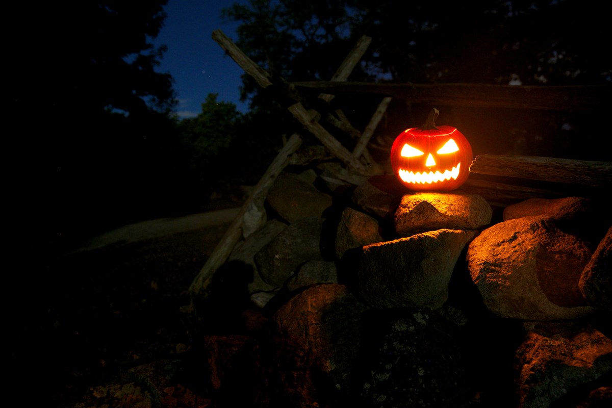 A glowing, orange jack-o-lantern with an evil face carving sits on a stone wall at night.