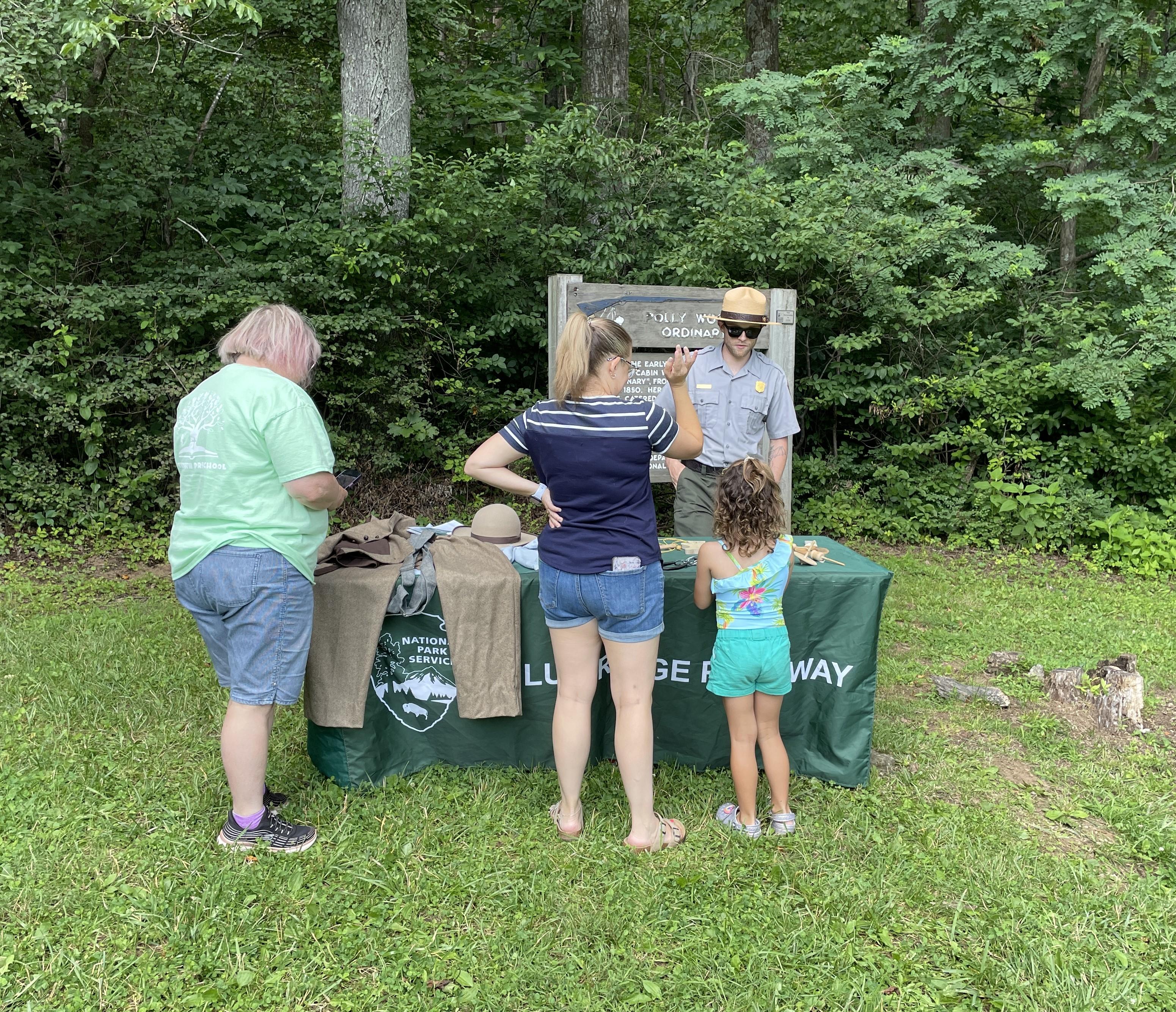2 adults and a child stand outside at a table with a uniformed ranger behind it