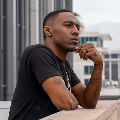 African American man leans against a balcony, chin rested thoughtfully on his hand.
