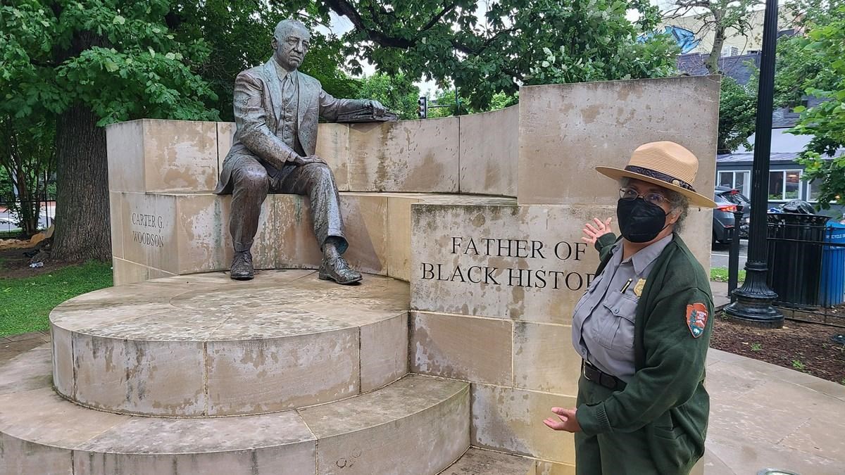 A ranger stands outside in front of a statue of Dr. Carter G. Woodson.