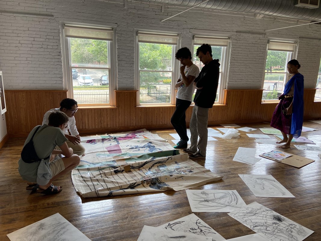 People gather around art laid out on the floor.