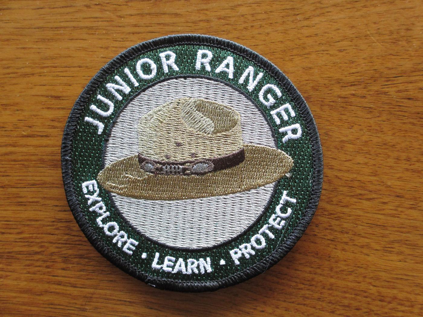 A color photo of a patch for the Jr. Ranger Logo with a grey flat hat and green boarder
