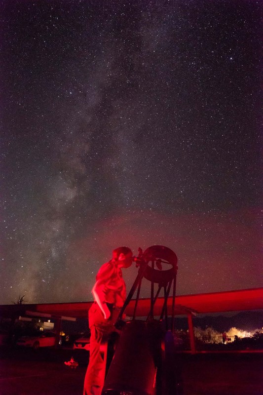 Night image of a person looking through a telescope with the Milky Way above