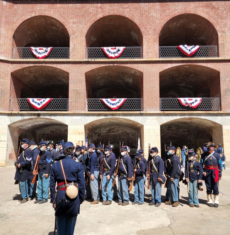 Reenactors standing on the parade ground in front of brick casemates with American flag bunting