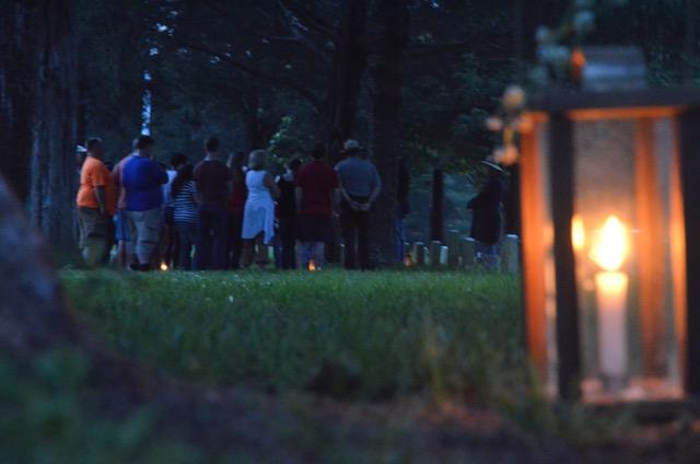 A ranger and visitors stand in the national cemetery with a candle lantern in the foreground.
