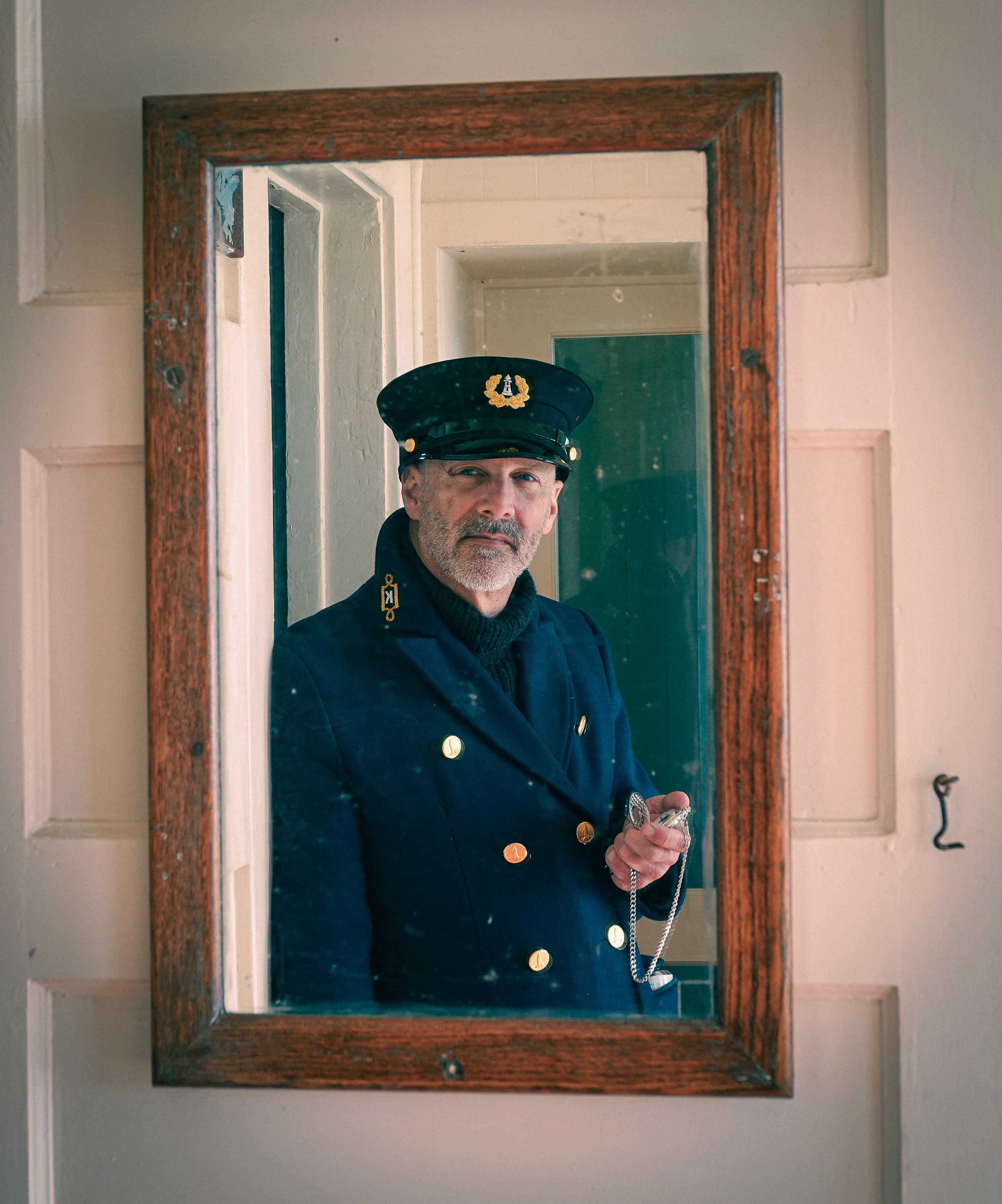 A lighthouse keeper looks into a wood-framed mirror