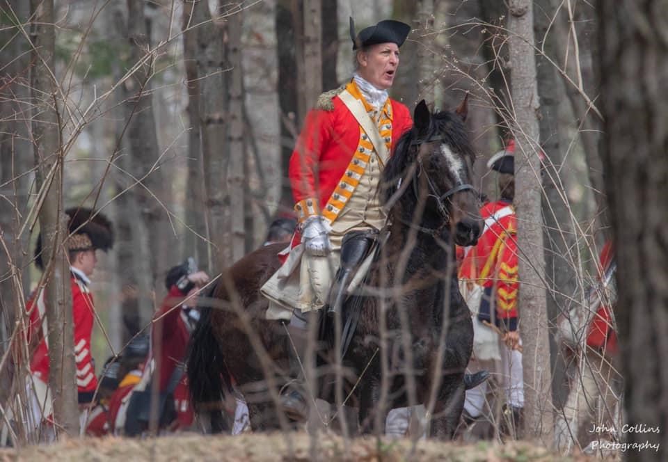 A Revolutionary War British officer in a scarlet coat on horseback in the woods.