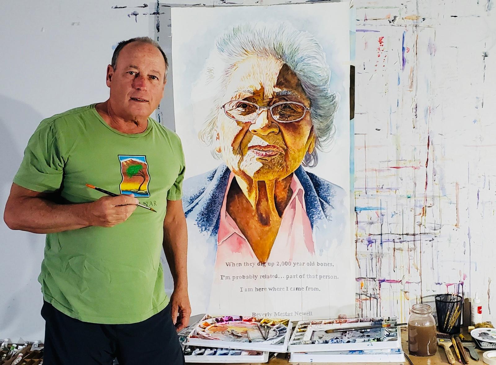 man with paintbrush stands next to a portrait of a woman