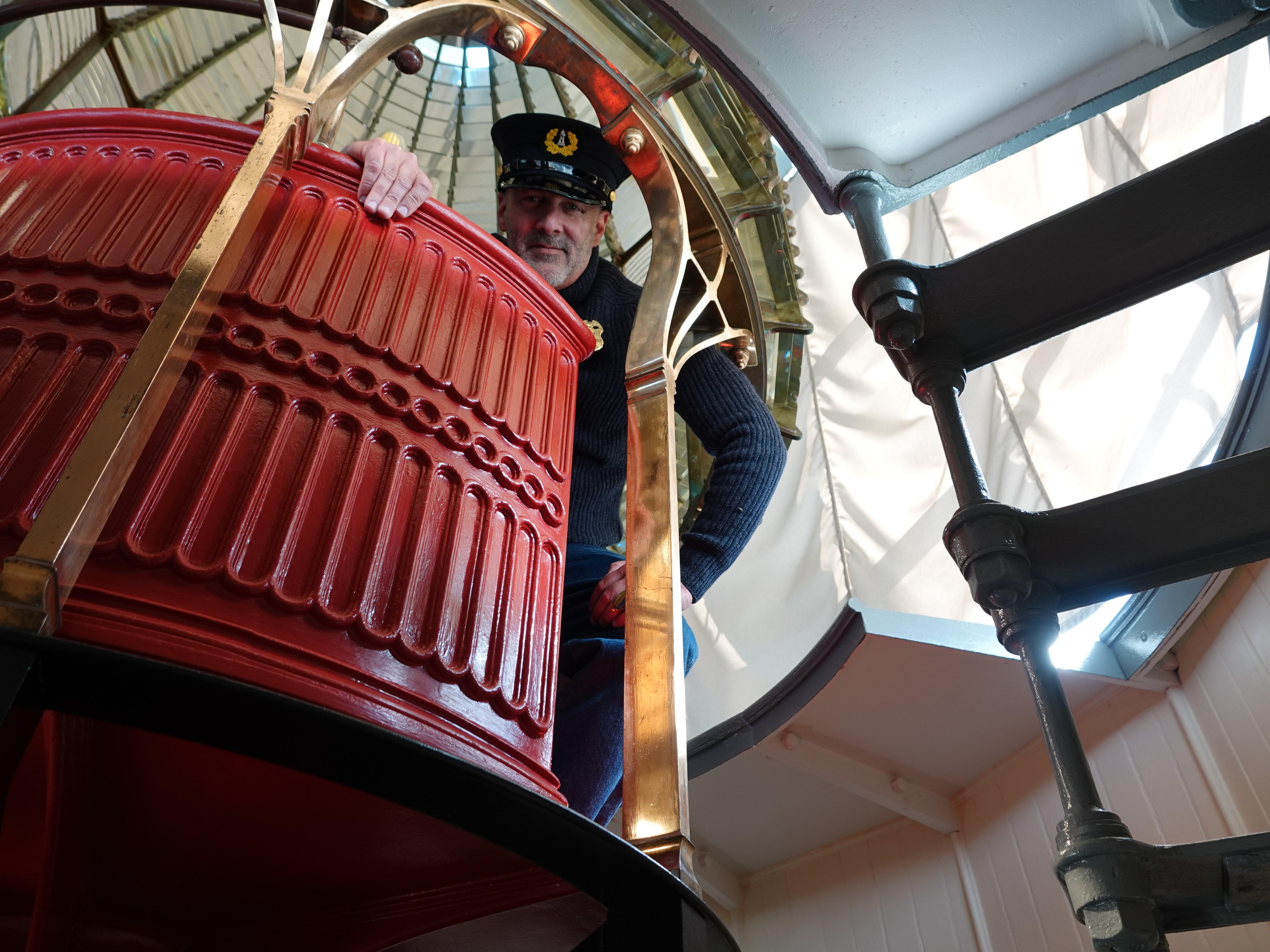 A lighthouse keeper pokes his head through an opening in a large fresnel lens.