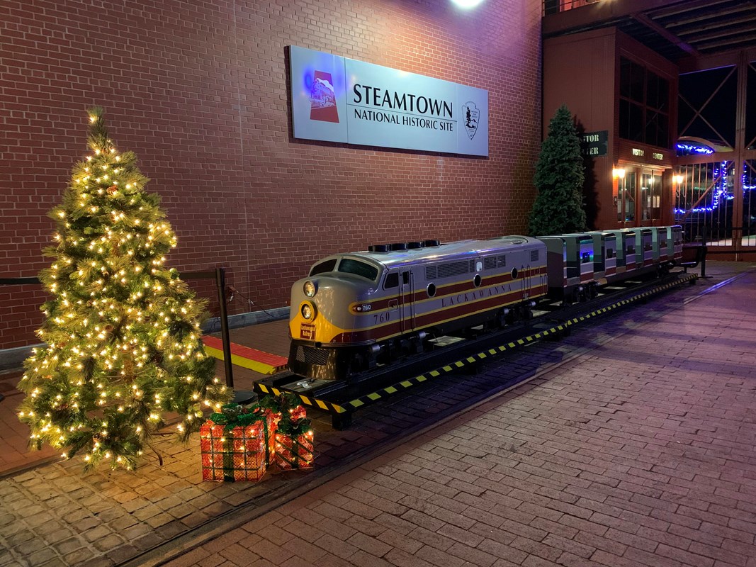 A miniature train on platform surrounded by holiday decorations.
