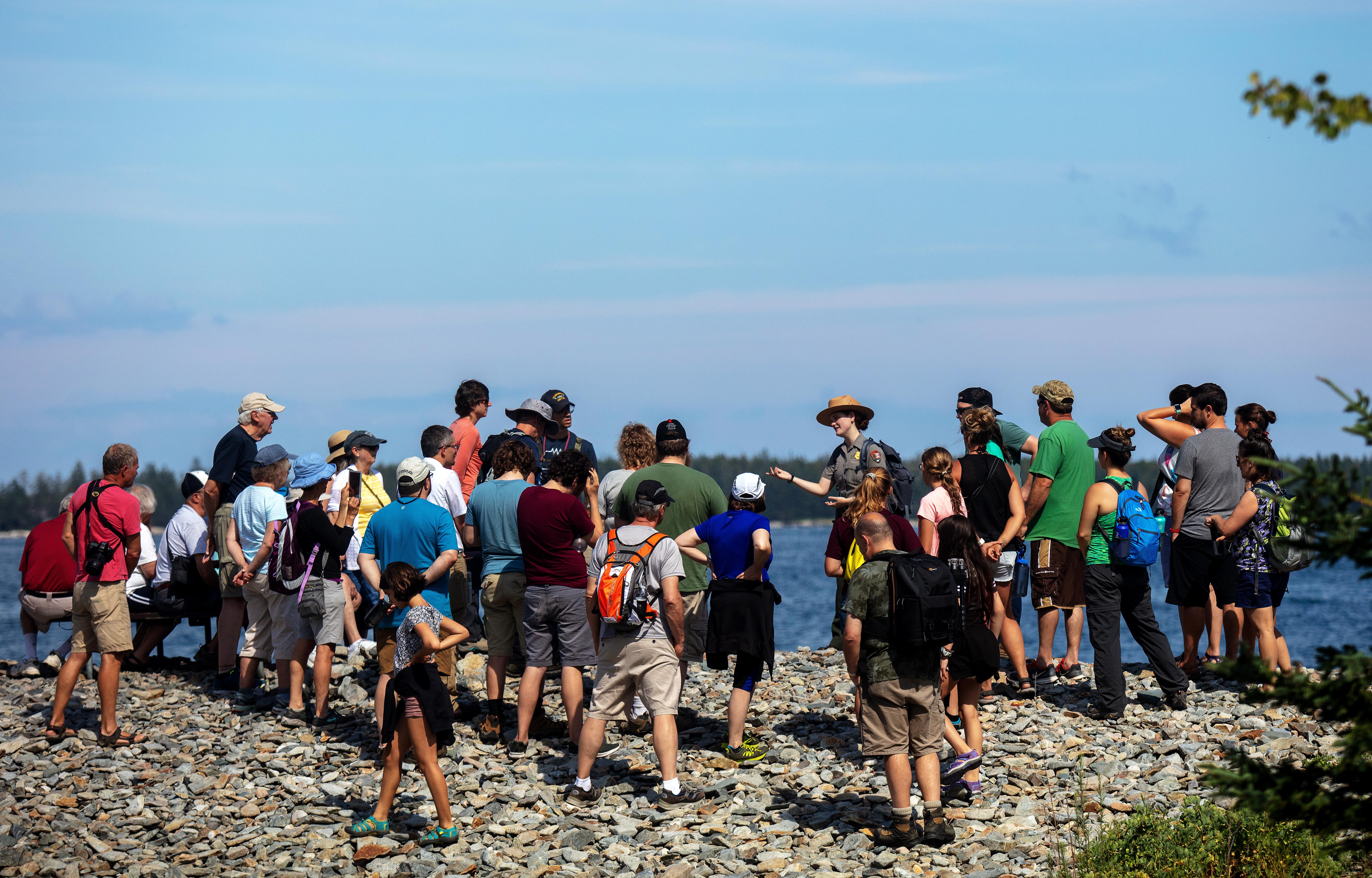 Group of people standing on a  rocky shore with a National Park Ranger.