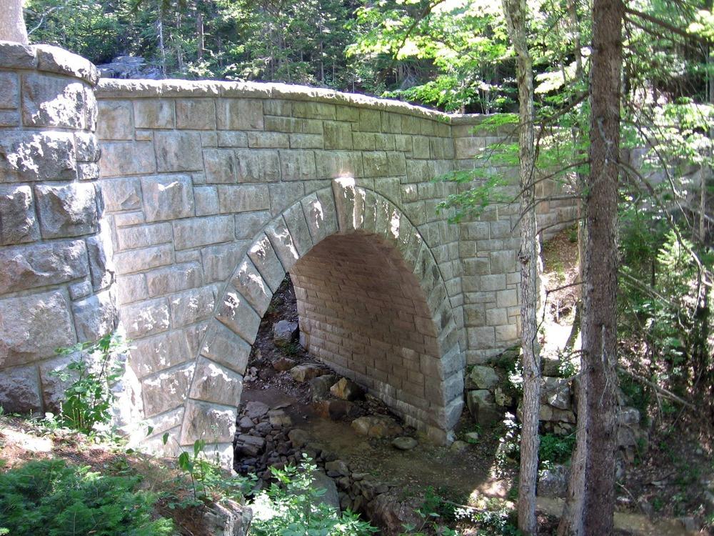 A stone bridge with a rounded arch in a forest.