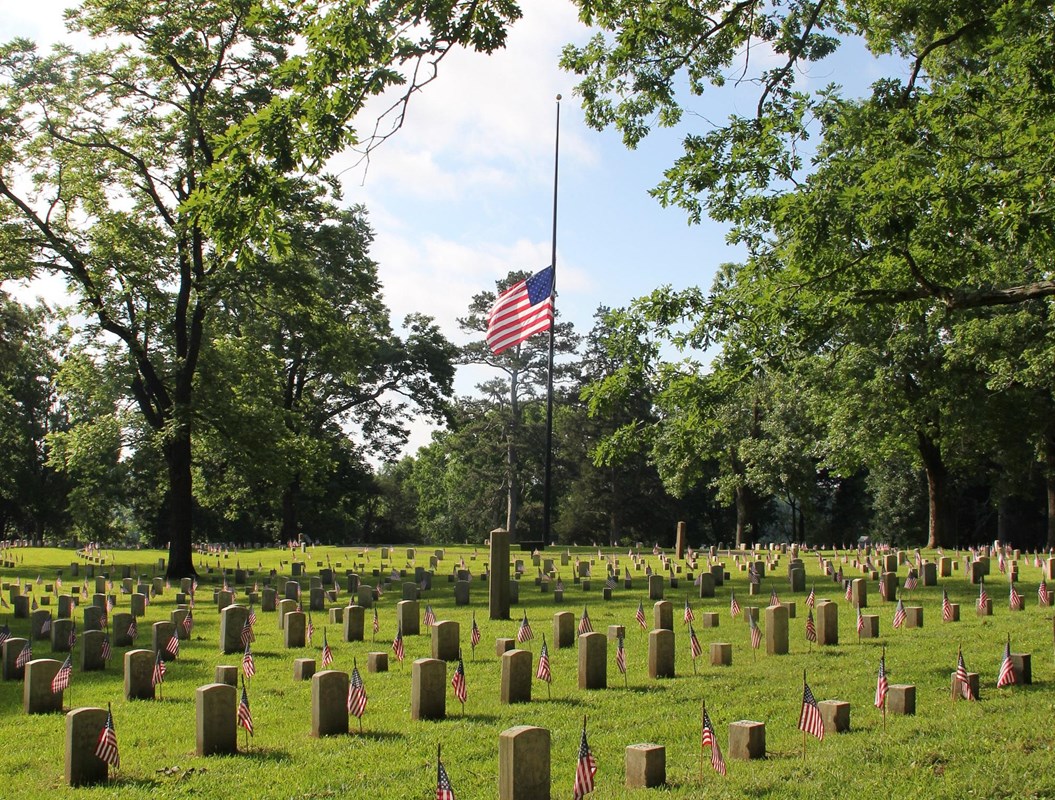 American flag flies at half-staff with headstones in the foreground.