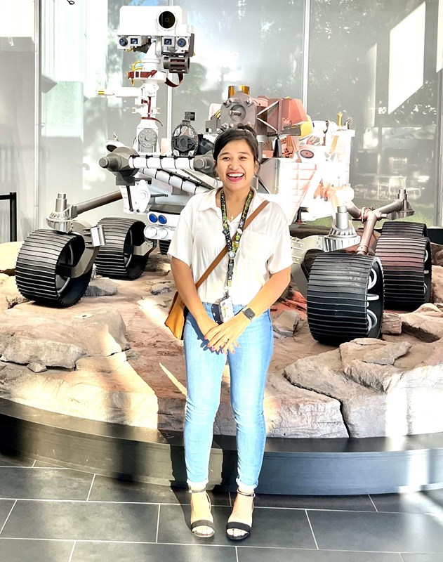 A woman standing in front of a space rover positioned on an exhibit that looks like rocks.