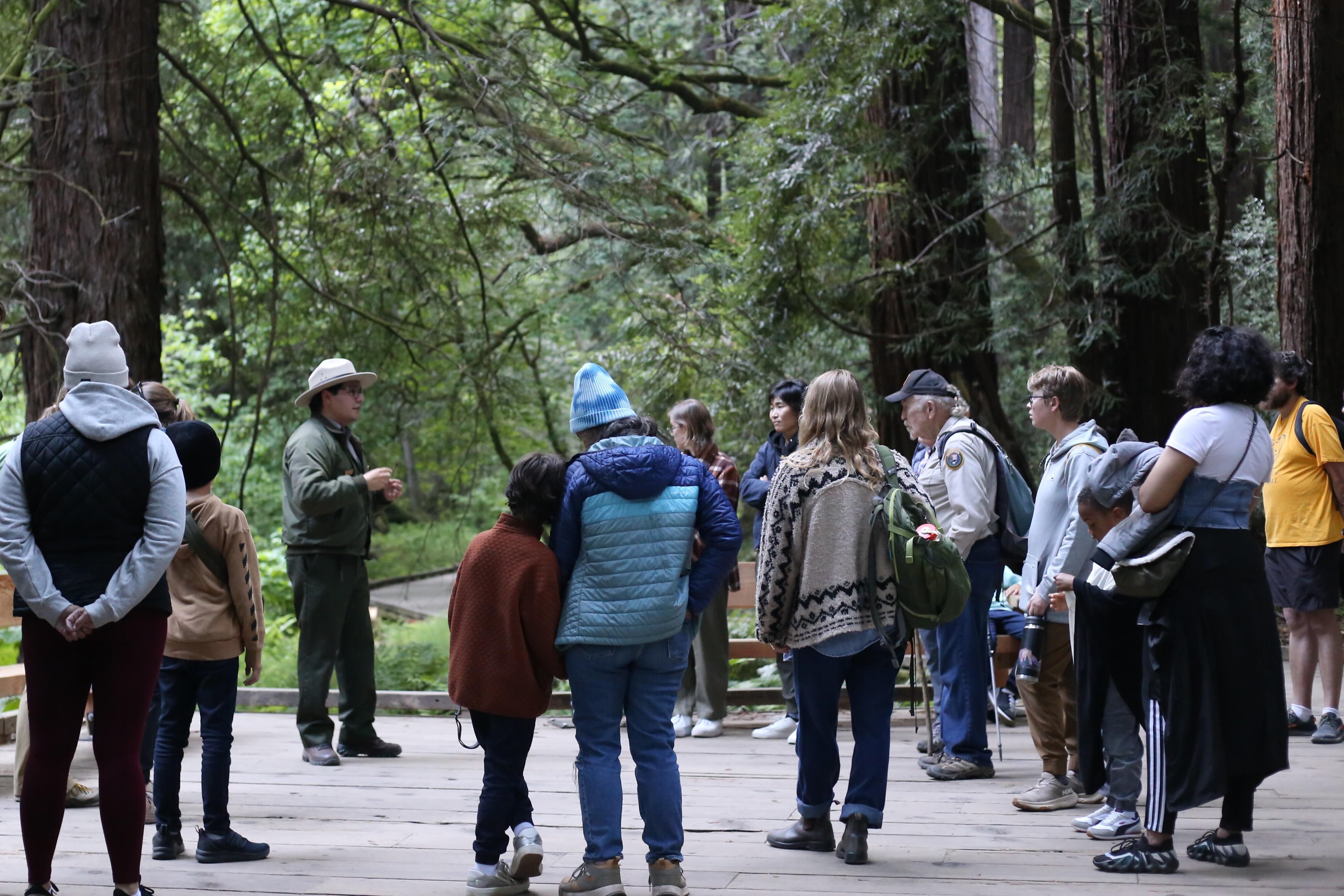 a ranger speaks with a group of people on a boardwalk in a forest