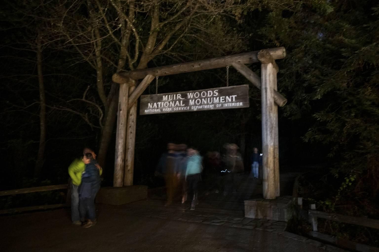 visitors hug in the dark under the muir woods entry arch