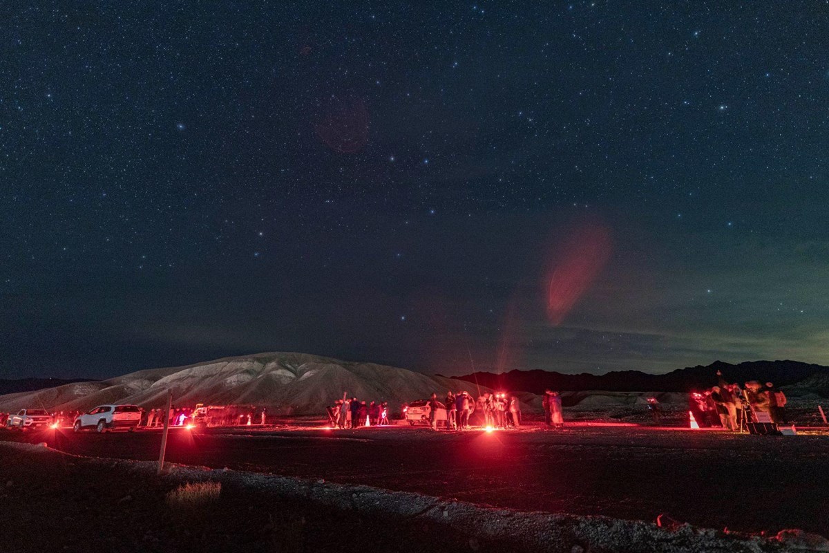 Visitors look through telescopes surrounded by red lights with the Big Dipper above the mountains