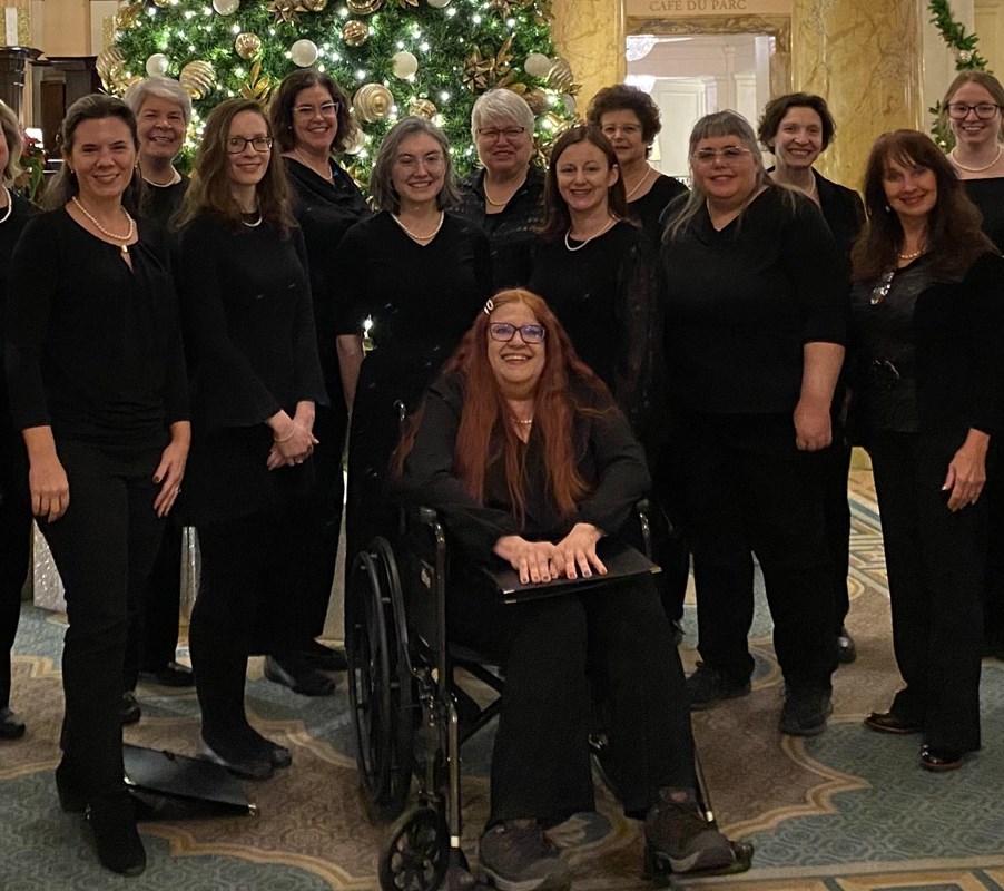 A group of 12 women stand behind one woman seated in wheelchair