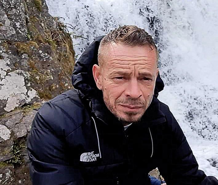 Portait of a man in a black park kneeling in front of a waterfall