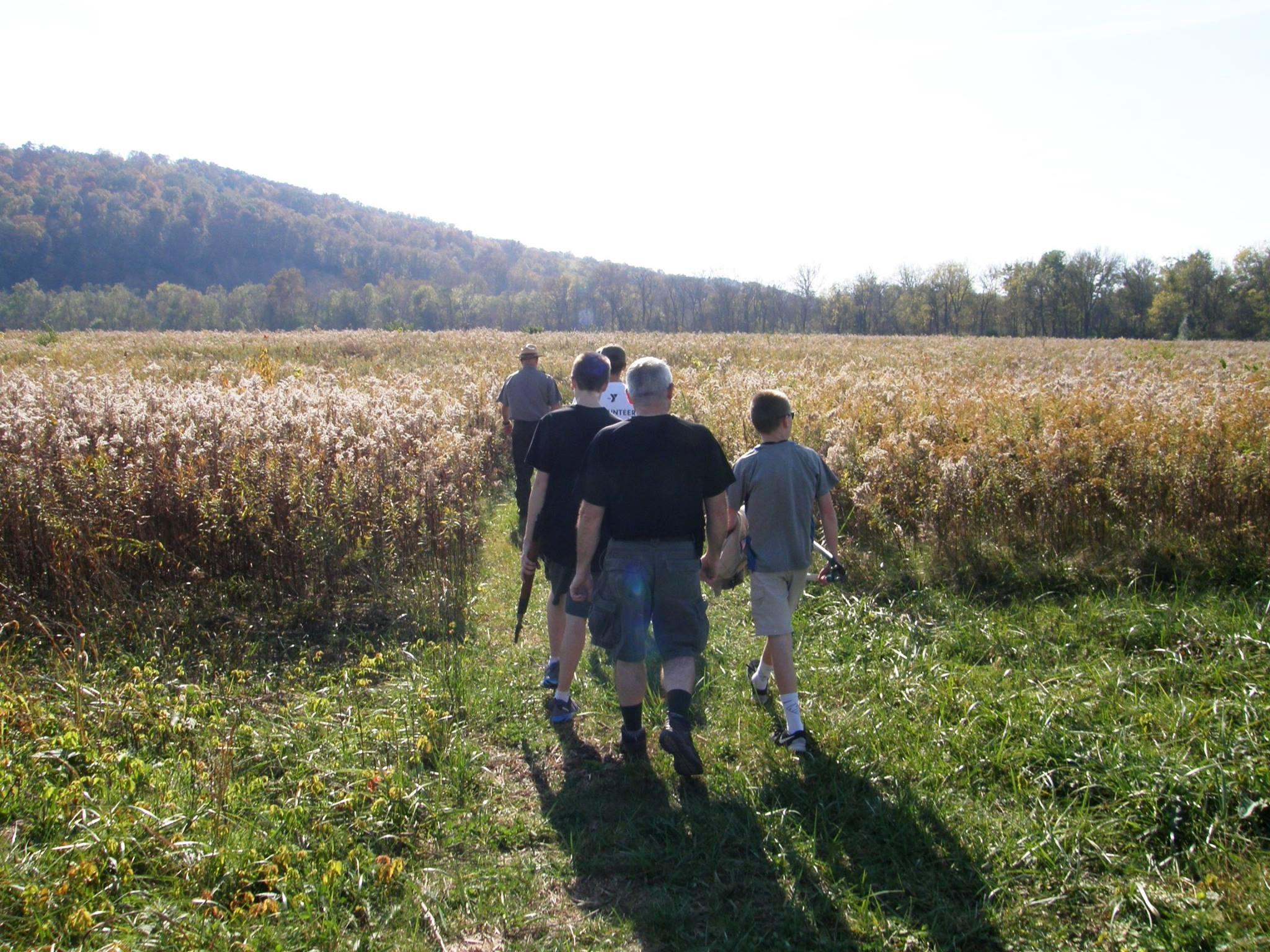 a group of people walk on a grassy path through a large field.