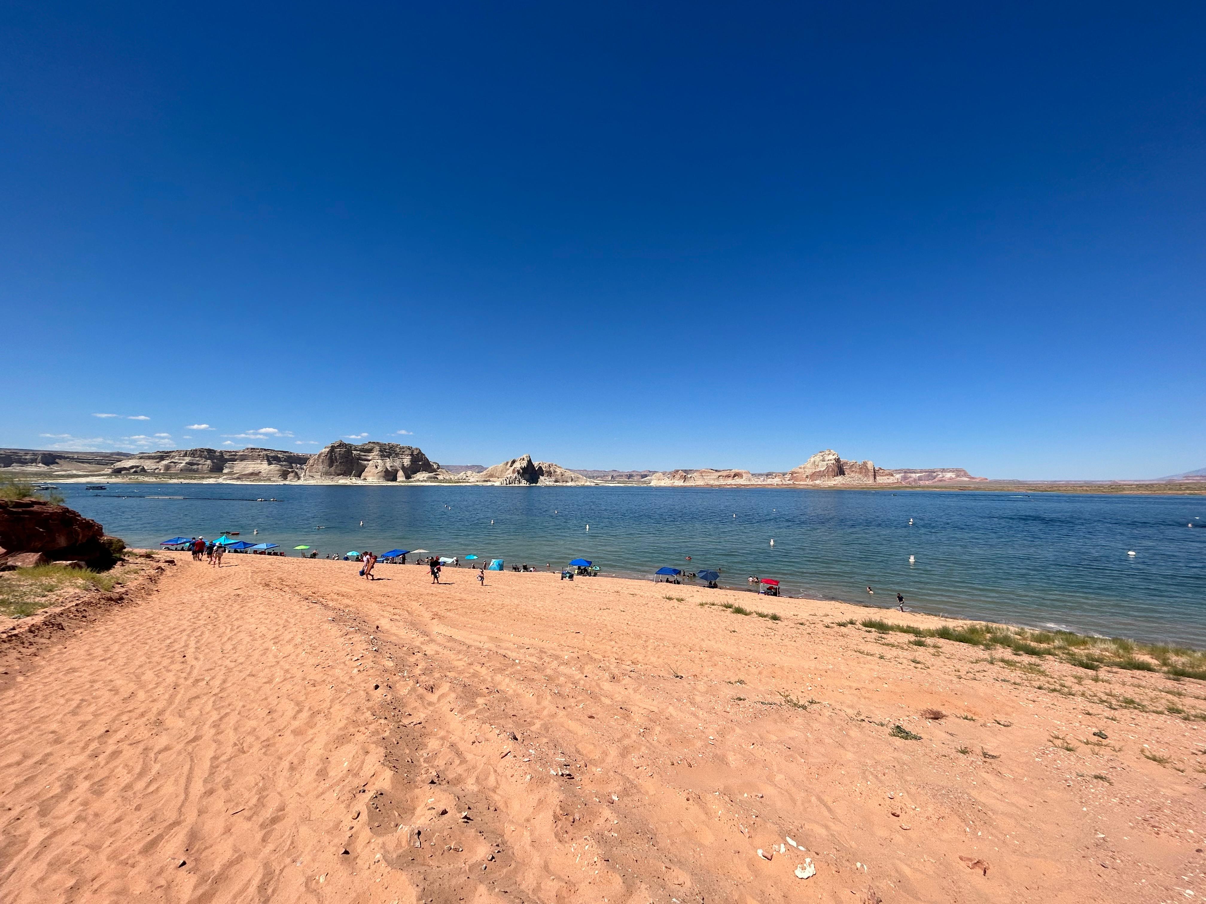 A sandy beach under a blue sky with people in the distance.