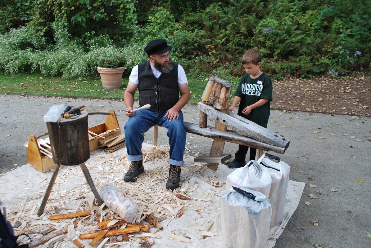 Woodworker surrounded by shavings and tools talks to young boy