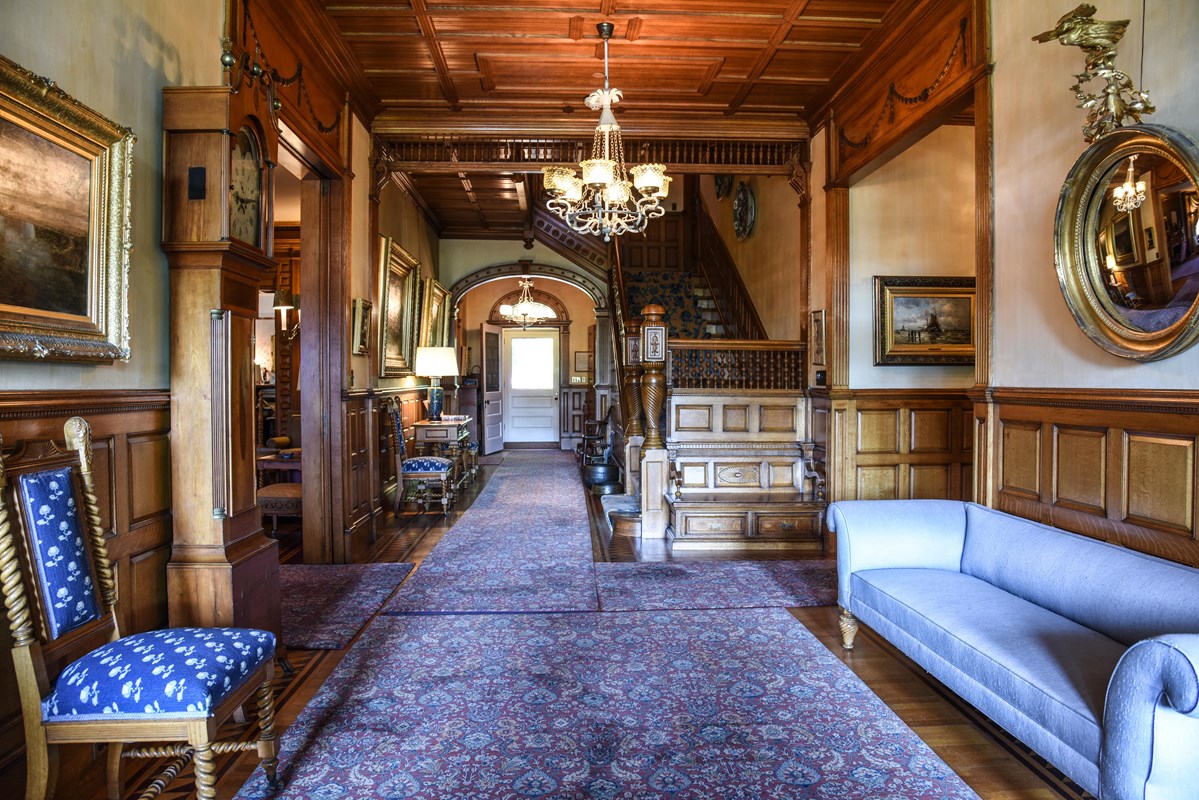 entrance hall of Victorian mansion, walls are paneled with ornate wood and paintings