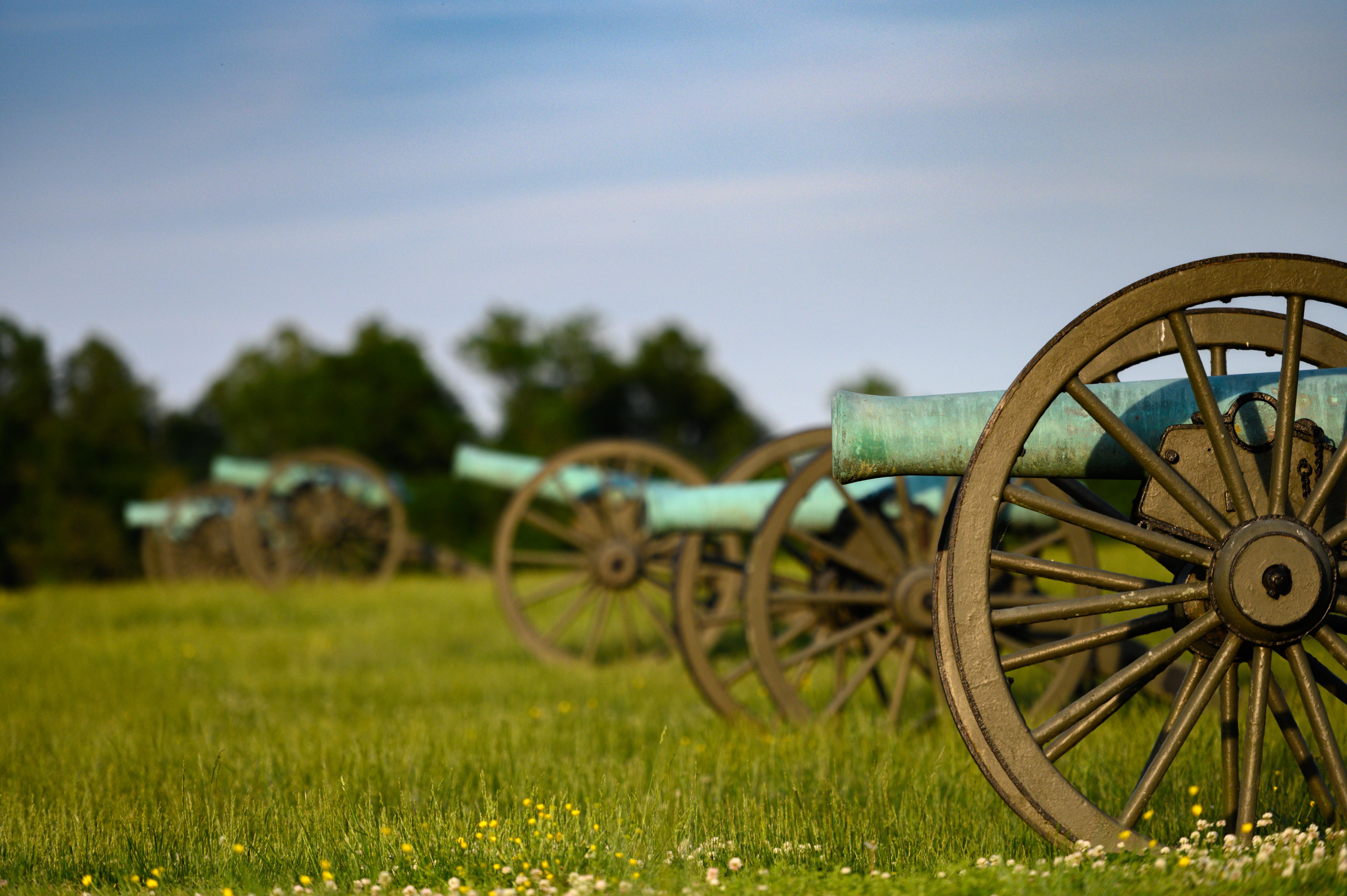 Five bronze Civil War cannons lined up side-by-side in a grassy field.