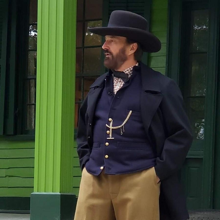 Man with dark hair and beard in black hat and navy blue frock coat