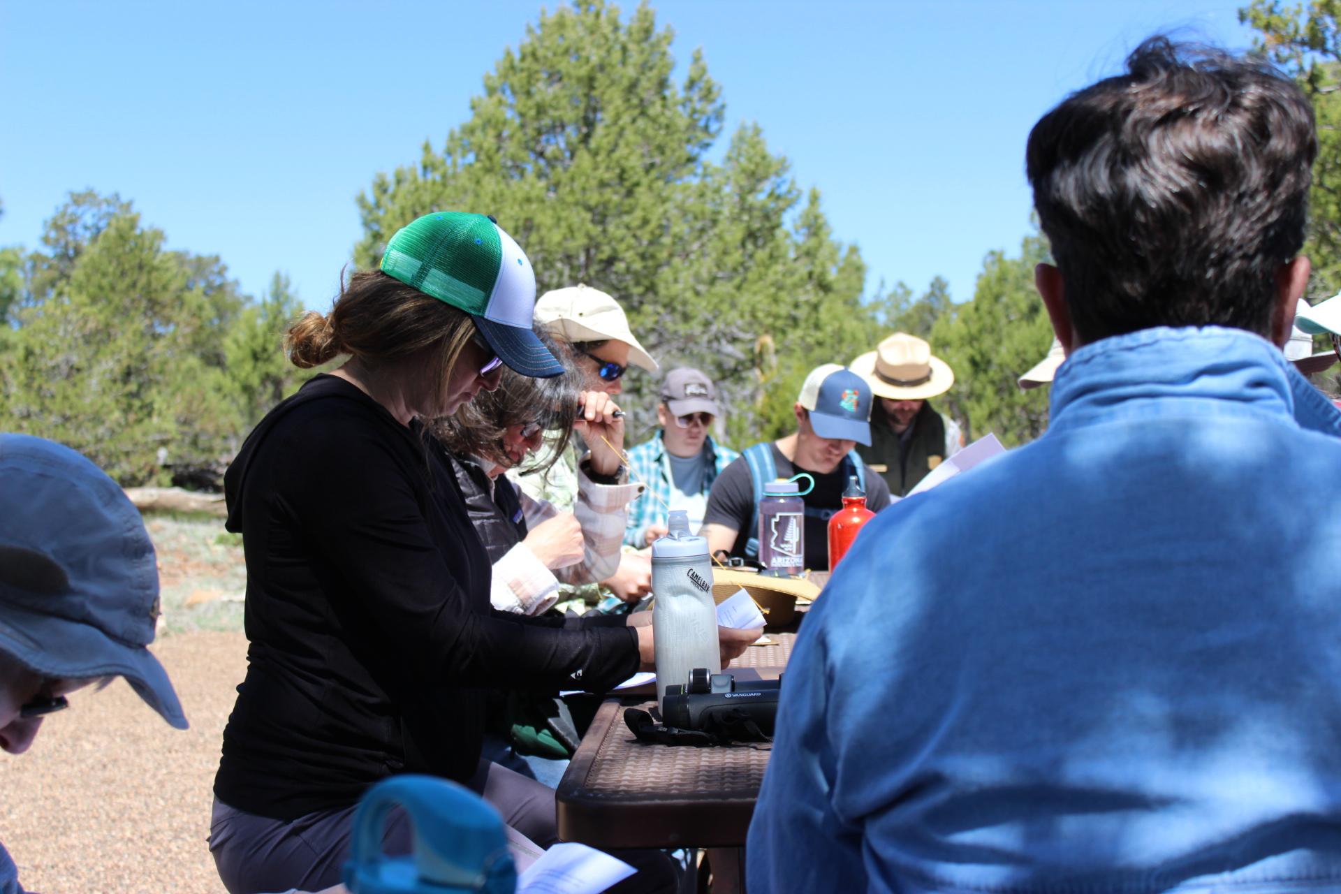 A group of visitors sit at a picnic table writing poetry with a park ranger