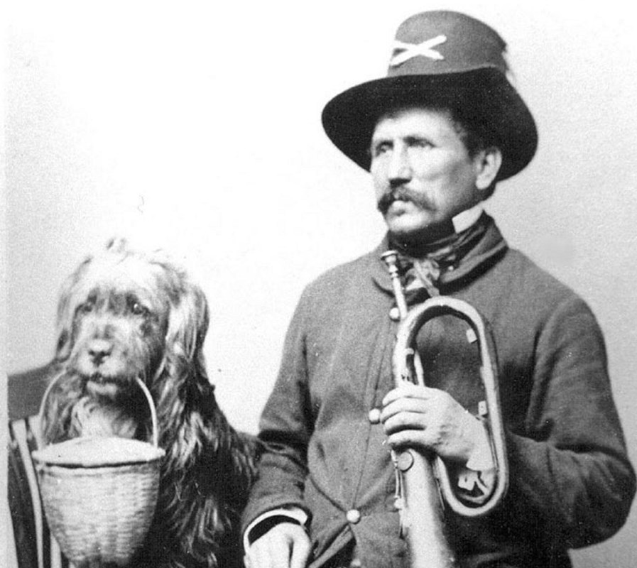 Historic black and white image of a Union soldier in uniform with a bugle sitting next to his dog