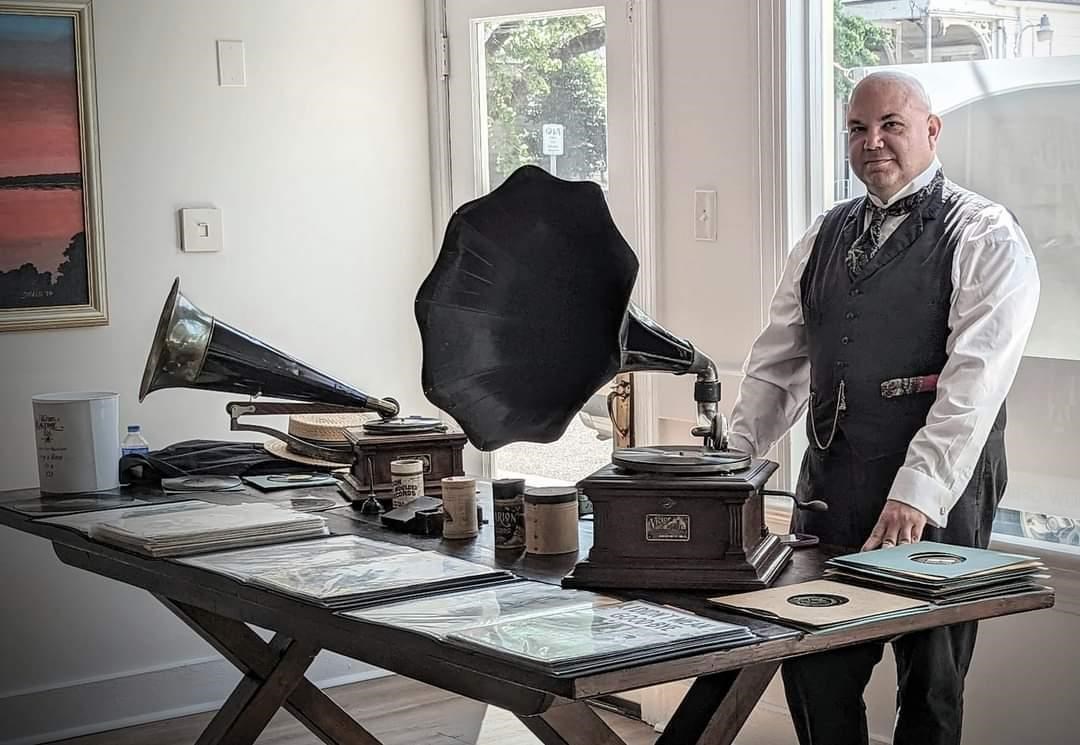 A man stands behind an antique wax cylinder recorder..