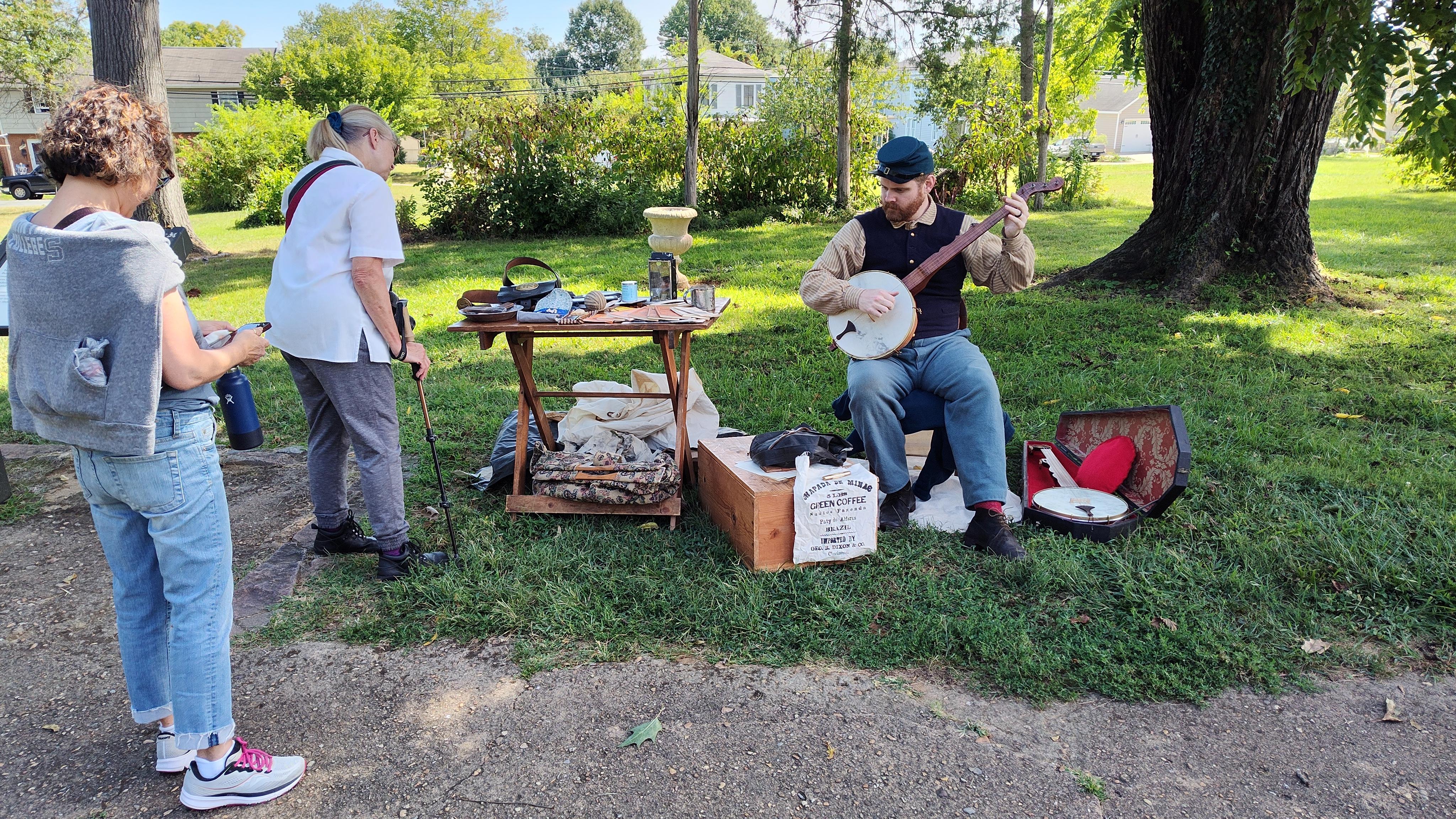 Volunteer Civil War reenactor in period clothing playing a banjo for visitors.