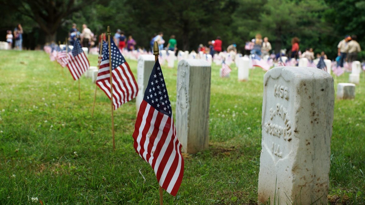 American flags stand in front of a row of national cemetery headstones.