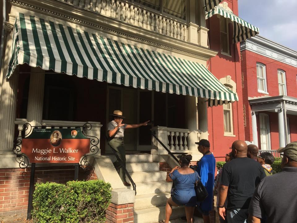 A woman in a Ranger uniform talking to a group of people from the front steps of a brick house
