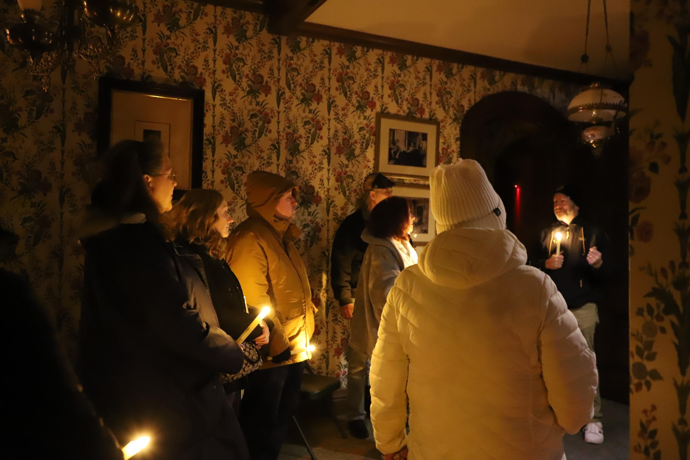 Visitors stand in a dark room in a Victorian home with candles.
