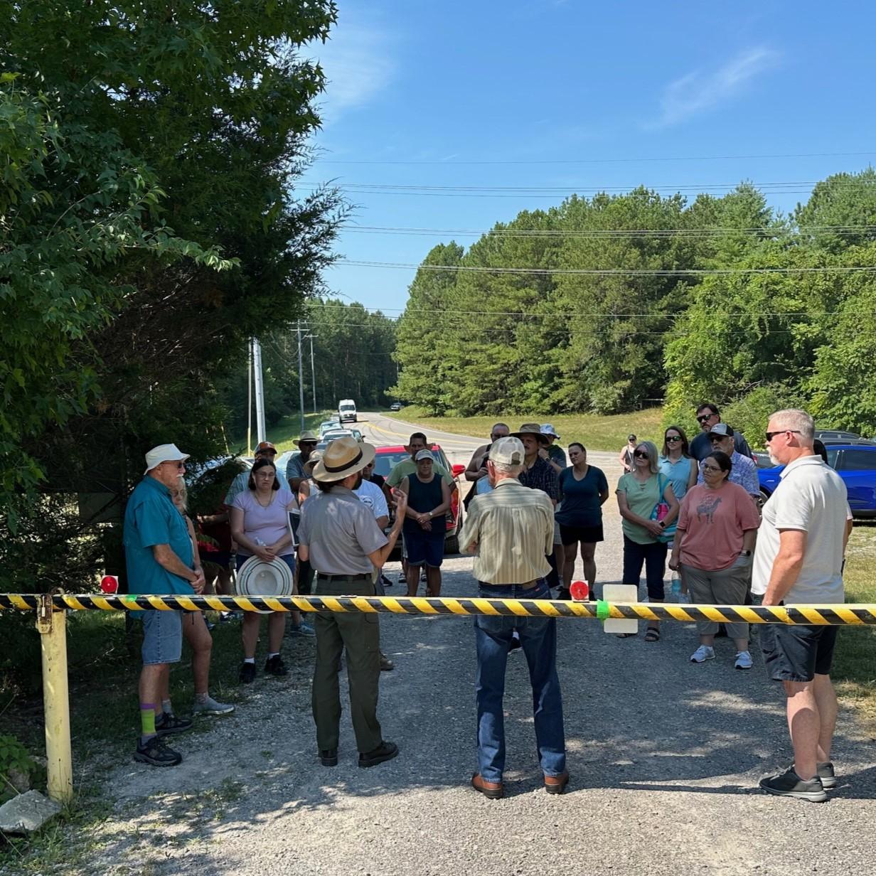 A park ranger stands with their back towards the camera surrounded by a large group of people.