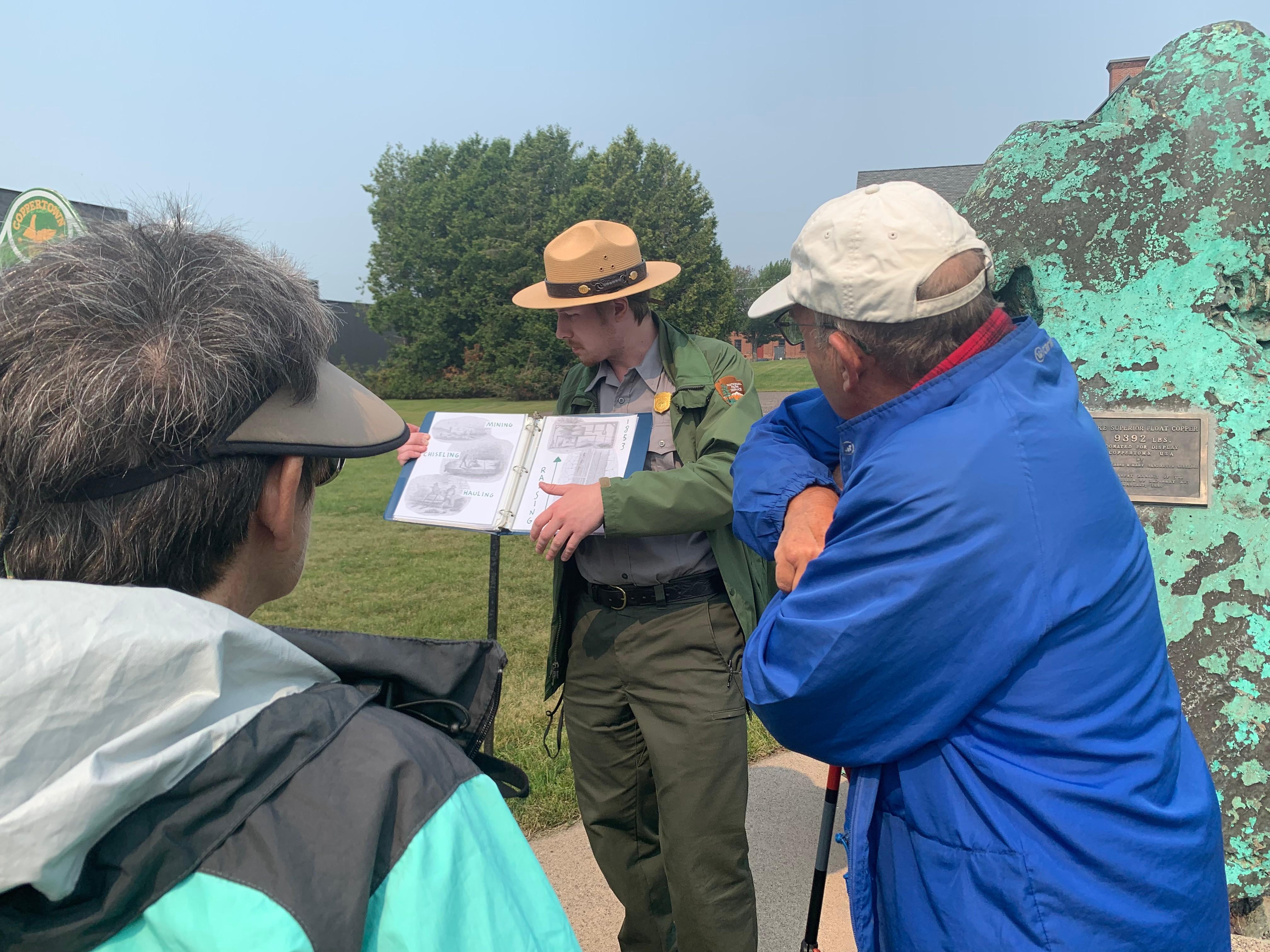 Visitors listening to a ranger program outside by a large green oxidized chunk of float copper.