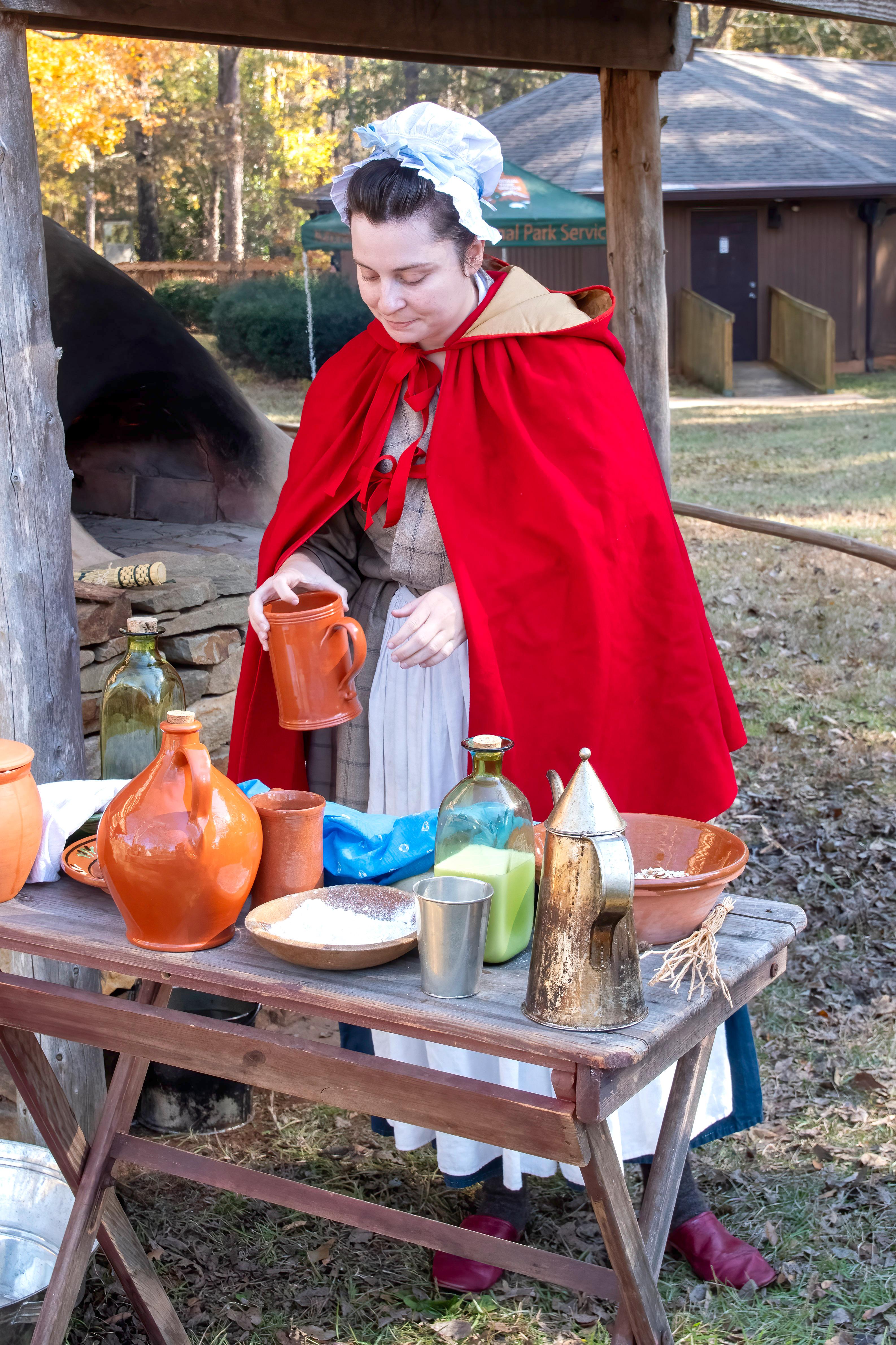 A woman in 18th century clothing is working with dishes.