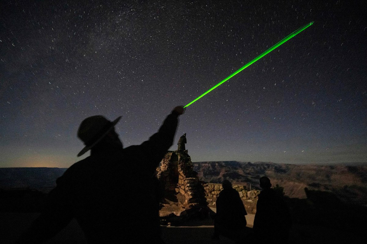 Silhouette of a park ranger using a laser pointer to point out constellations in a stary night sky.