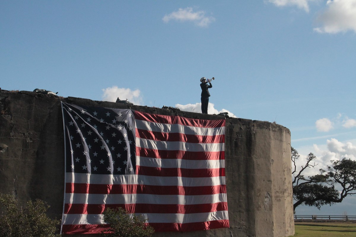 JROTC Cadet plays TAPS on top of Battery Church with  large US flag draped on the battery.