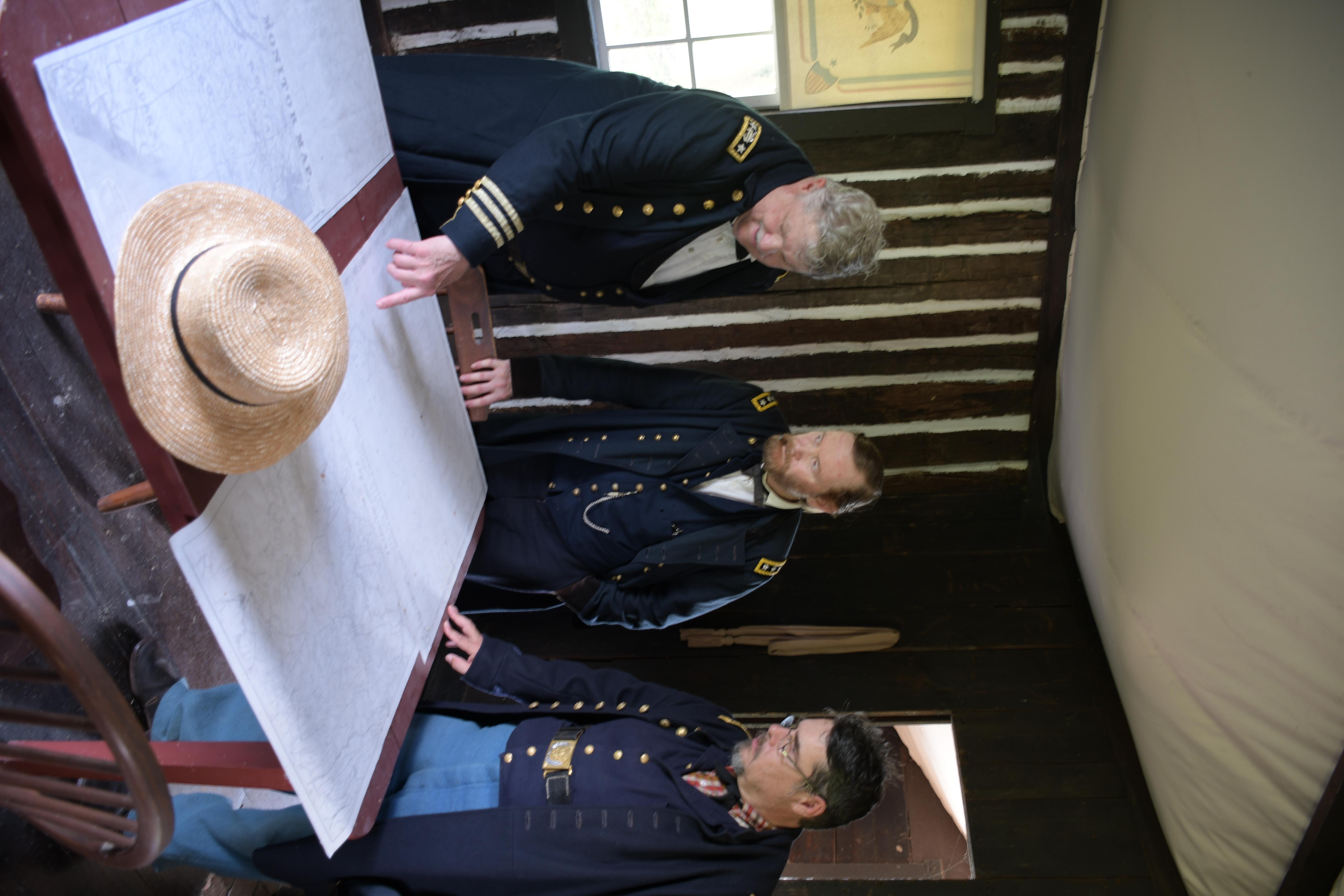 Three men wearing US Civil War officer uniforms stand together looking at a map.
