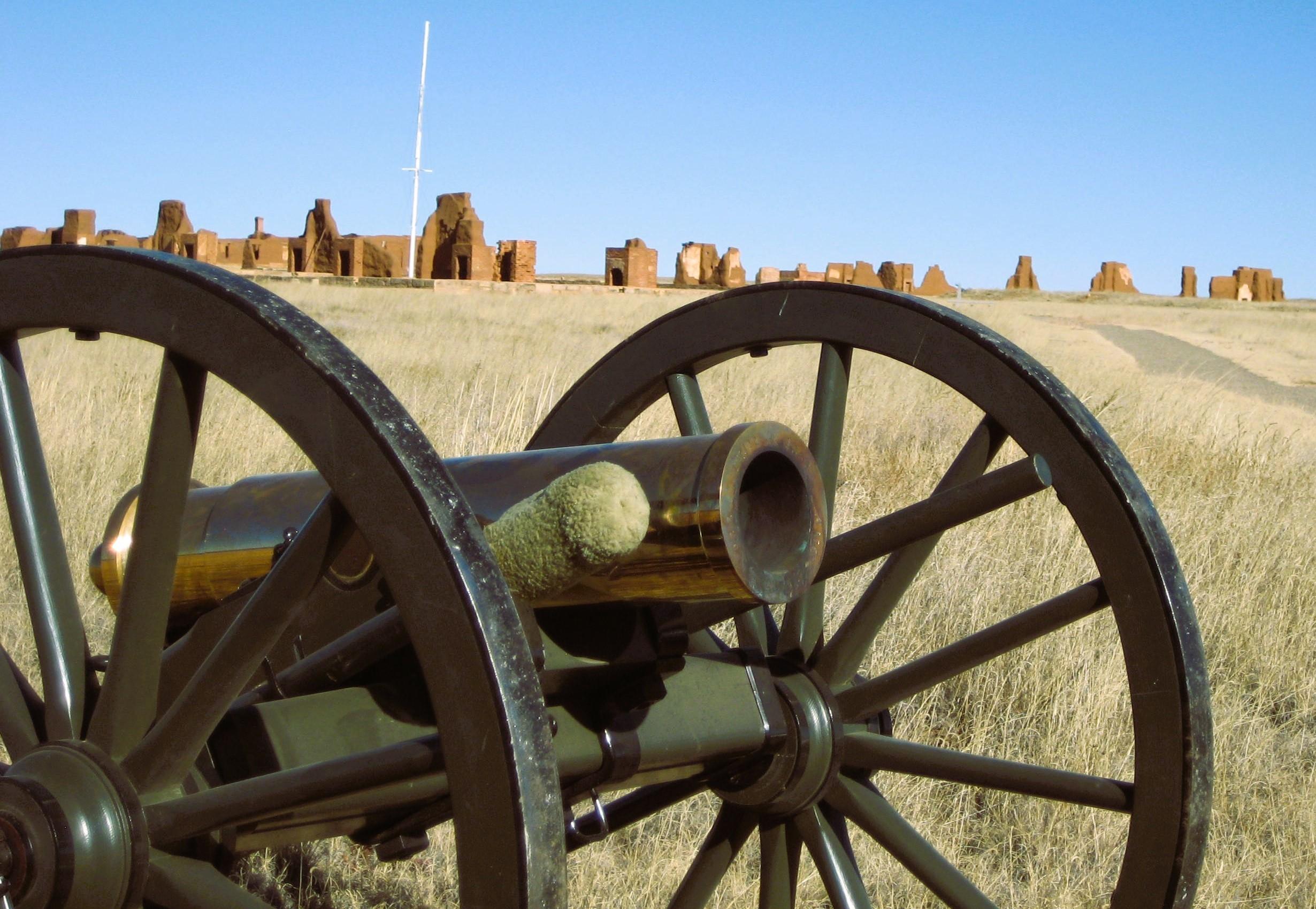 A howitzer and carriage with the adobe ruins of the third Fort Union beyond.