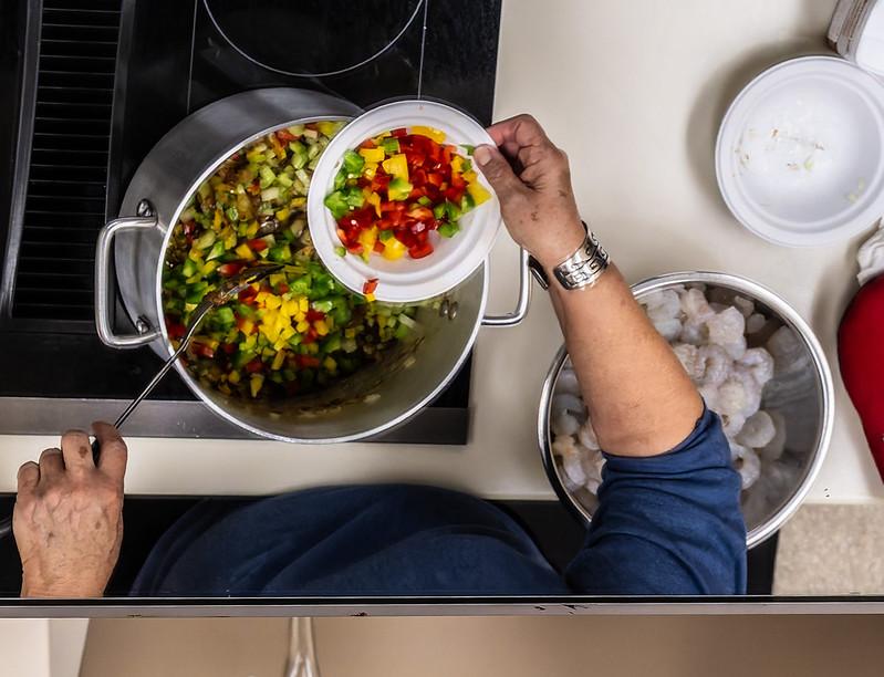 A look from above at a pot cooking colorful vegetables while a cook adds more and stirs.