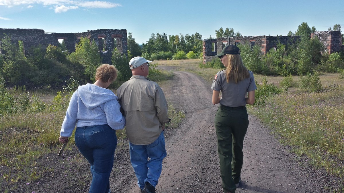 A ranger talks with two people as they walk together towards a historic building.