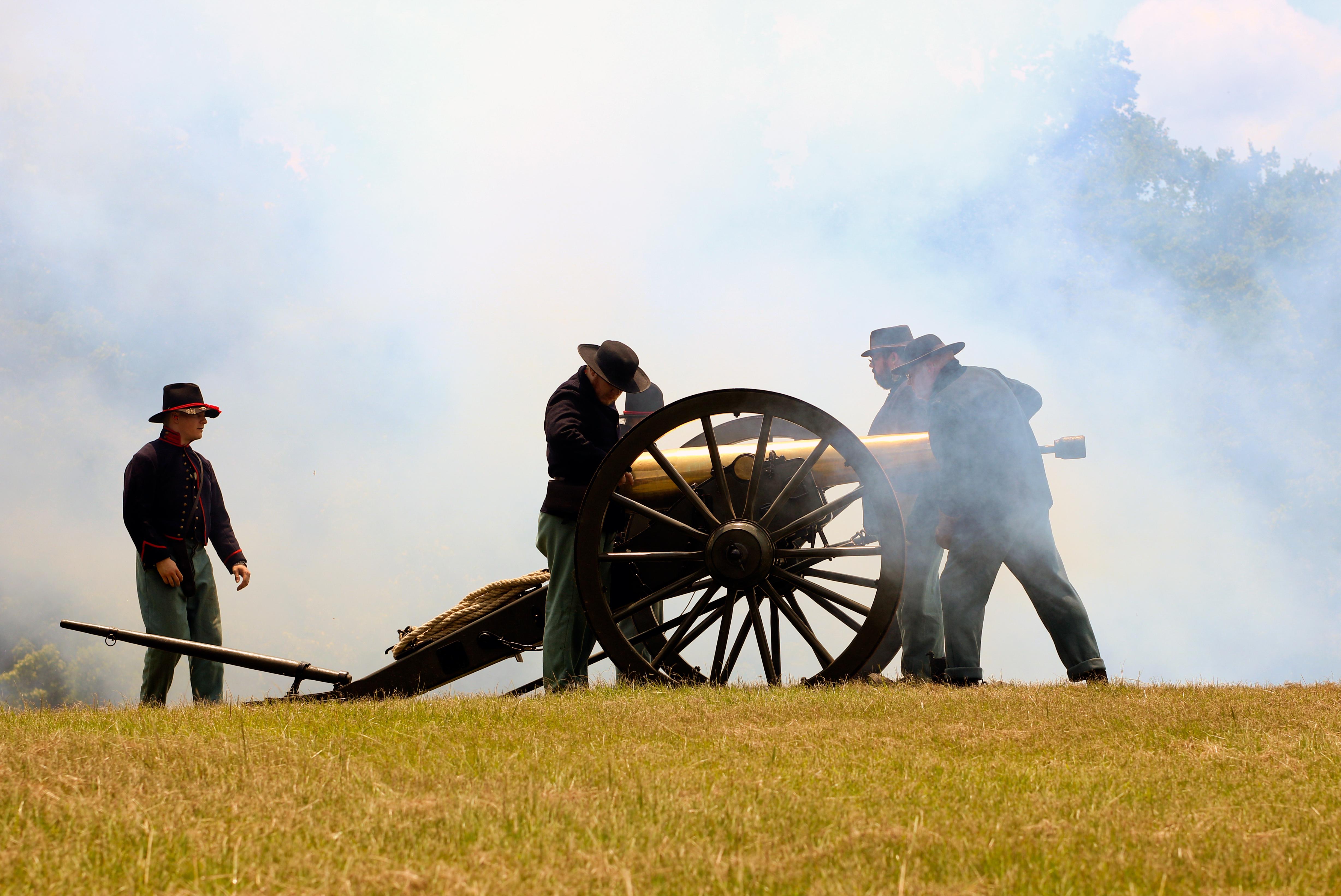 A cannon crew loads a gold-colored cannon as smoke fills the air