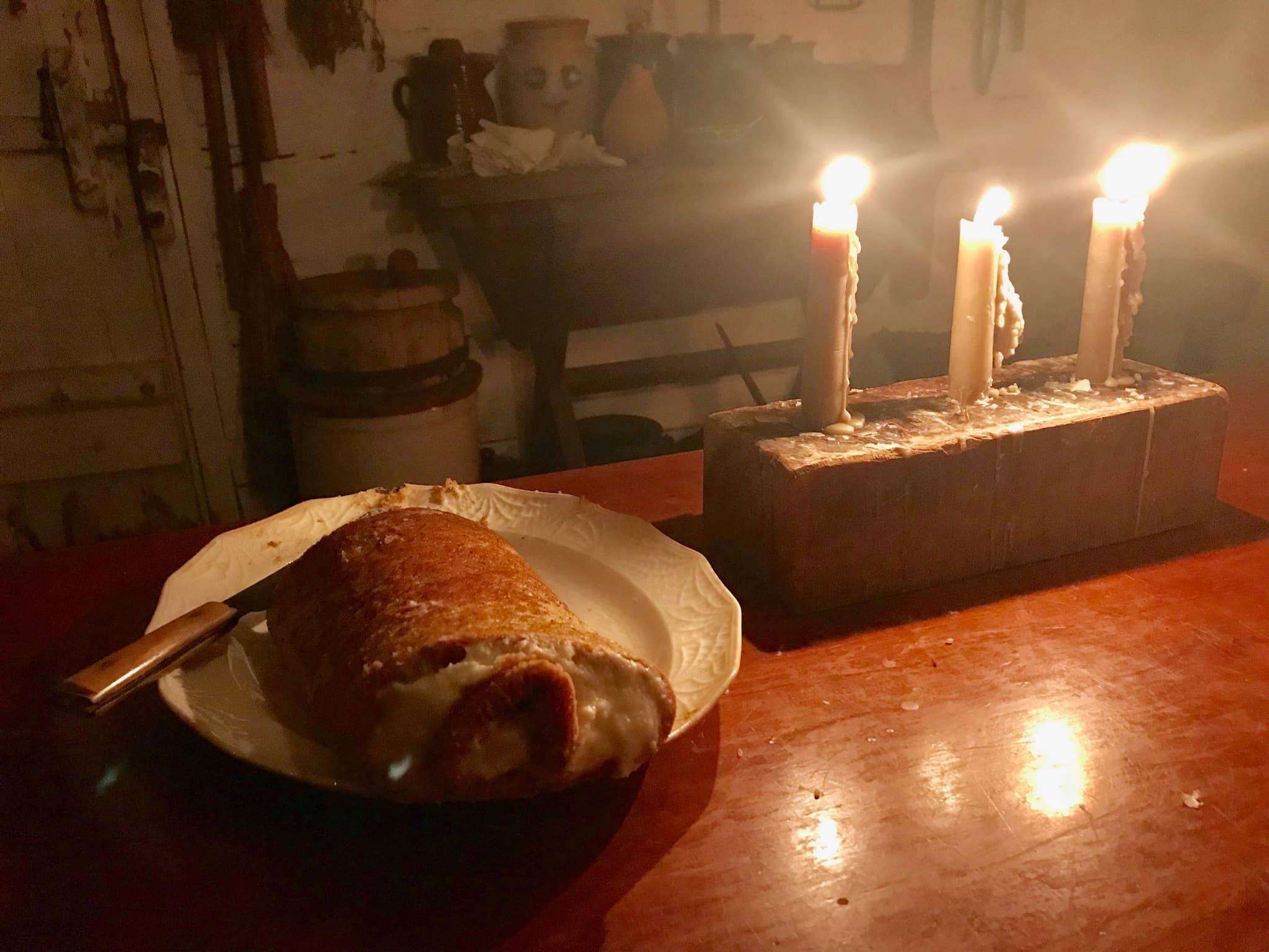 Three candles illuminate a dark room near a plate of food.