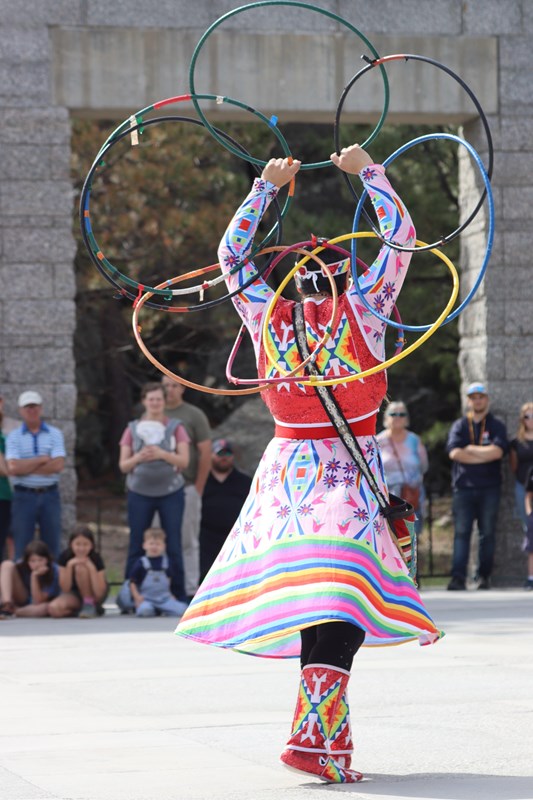 person in brightly colored clothing holding a dozen hoops in a circular pattern.