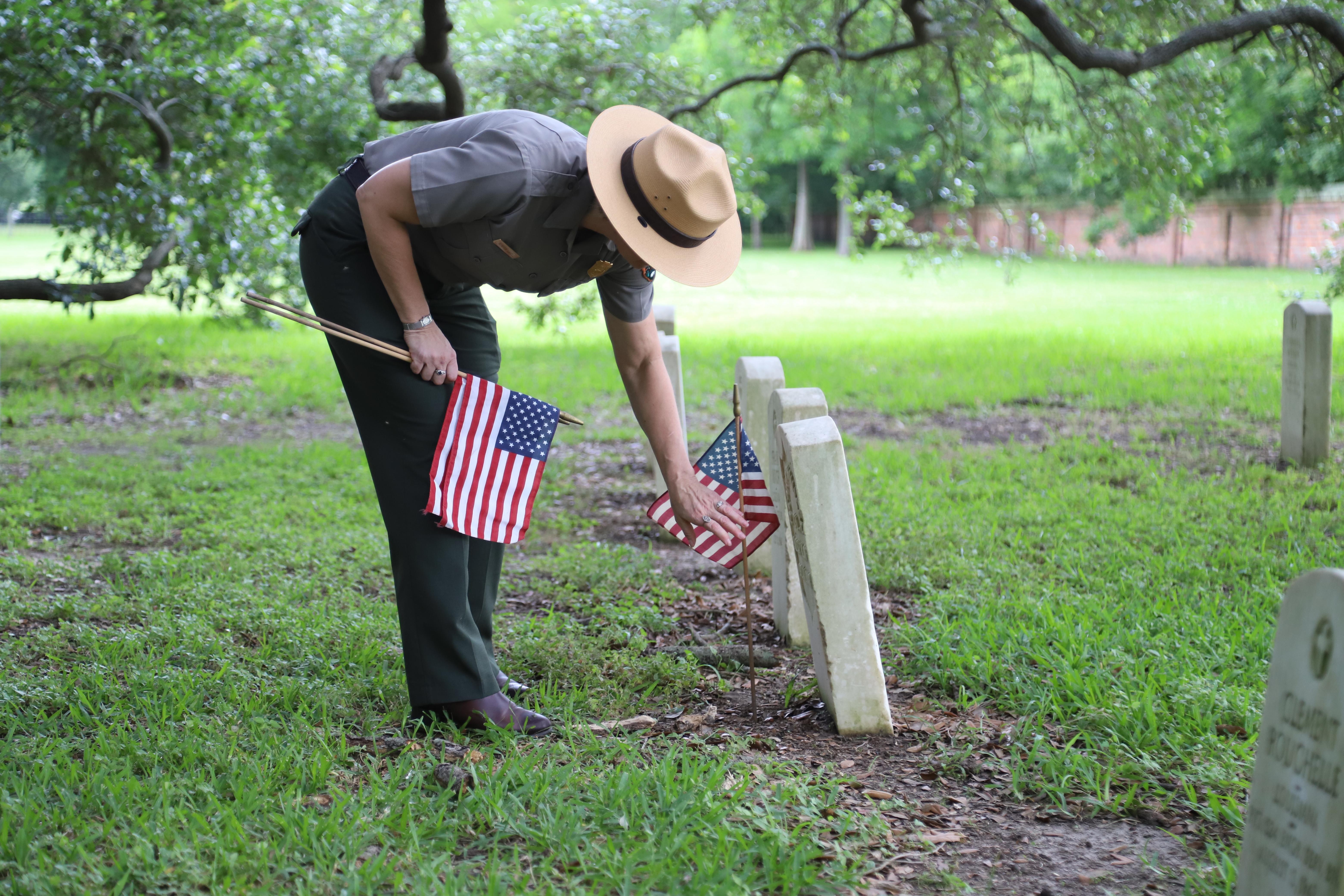 A ranger places a small United States Flag in front of a headstone in Chalmette National Cemetery.